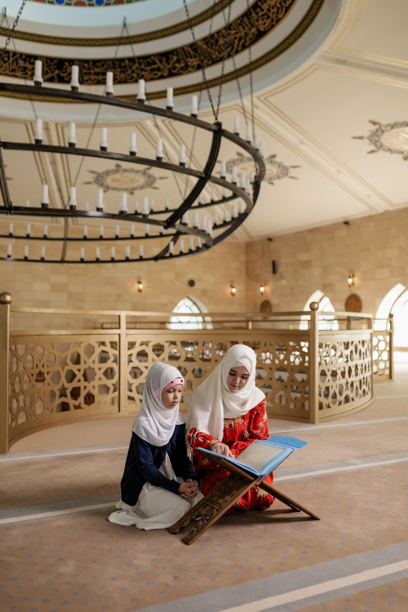 A female Qur'an tutor reading with a young student inside a mosque